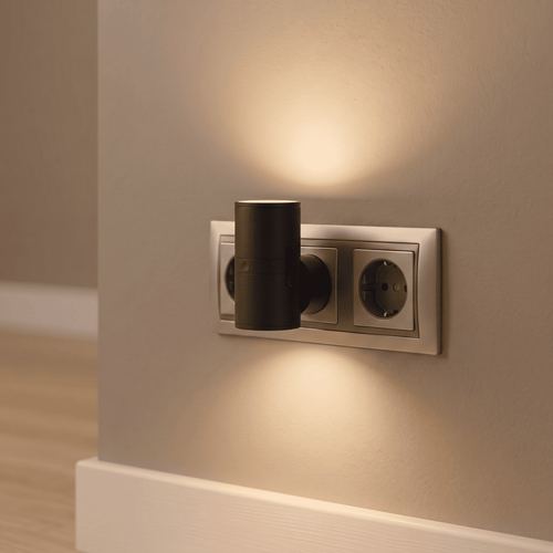 BoreaLight negra, luz cálida de enchufe con sensor, encendida en una pared al anochecer